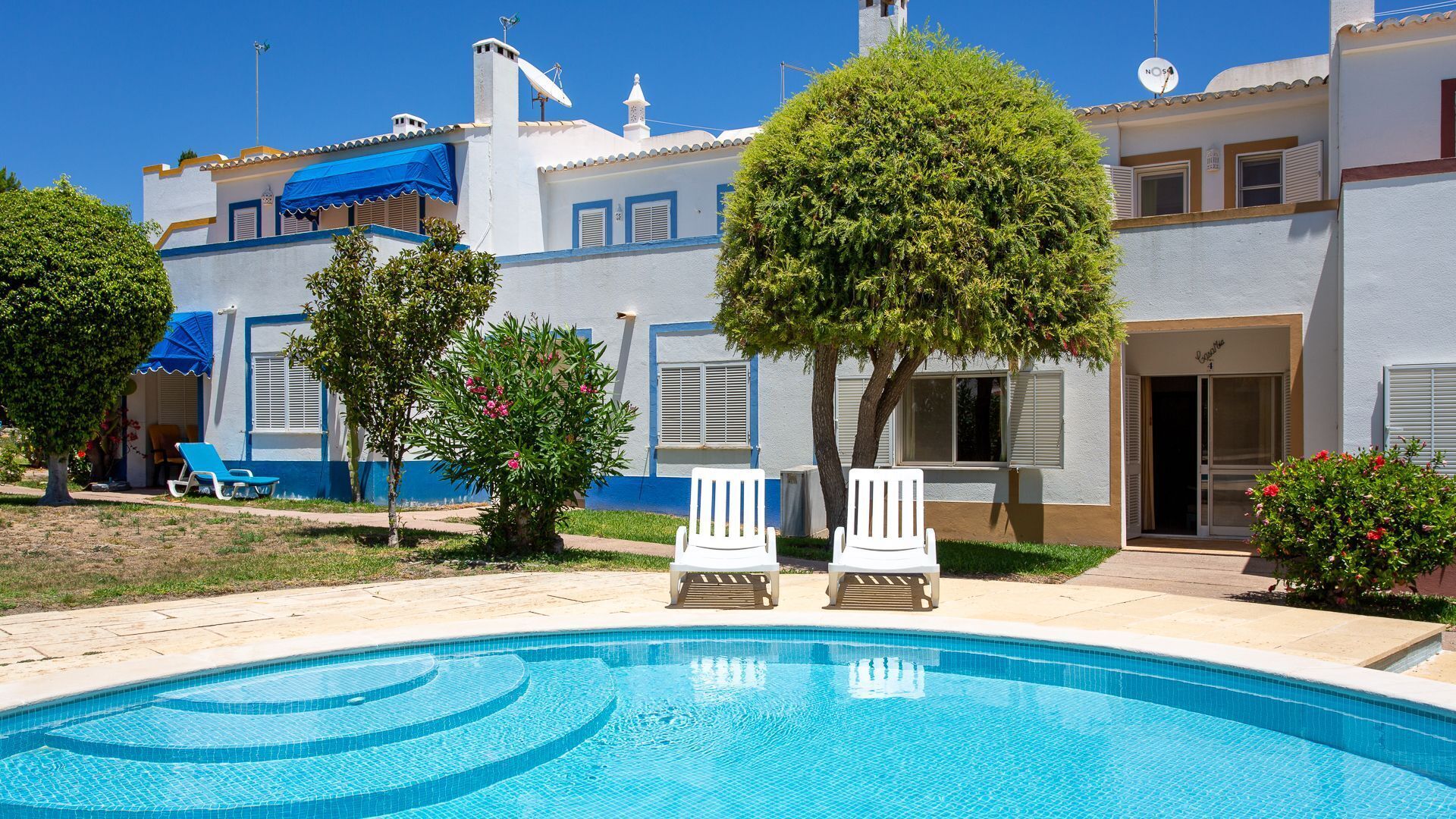 A swimming pool with lounge chairs, a building with blue trim, and a tree.