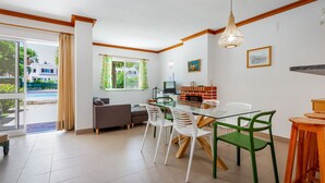 Een moderne woonkamer met een glazen eettafel, groene en witte stoelen, een bank en een televisie.