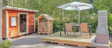 Eine Holzterrasse mit Gartenmöbeln und einer Uhr an einem kleinen Gebäude.