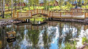 Un puente de madera sobre un estanque con un muelle de madera, rodeado de árboles y casas.