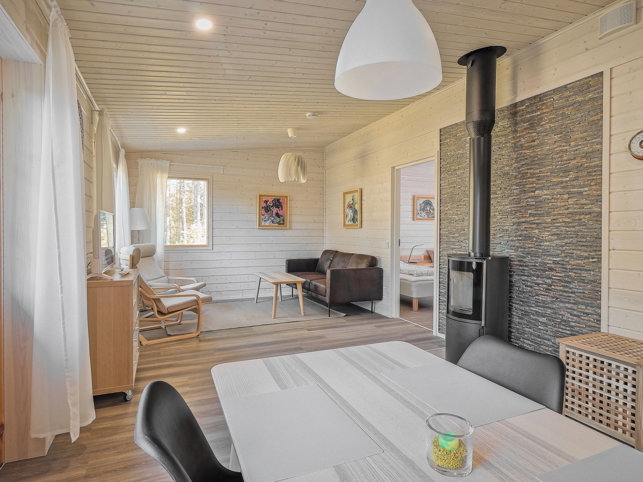 Een gezellige woonkamer met een open haard, houten wanden en een eethoek met een tafel en stoelen.