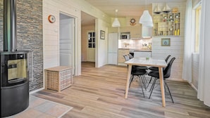 Een moderne keuken met witte kastjes, een eethoek met een houten tafel en stoelen, en een zichtbare kookplaat.