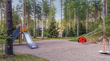 Un parque infantil con un tobogán y una decoración de mariquita roja en un área boscosa.