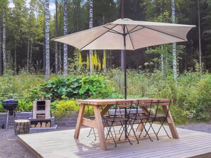 En träaltan med ett bord och stolar, ett parasoll, en grill och en tegelugn.