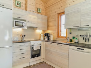 Une cuisine avec des meubles de rangement en bois, un four à micro-ondes encastré, un four traditionnel et une fenêtre.