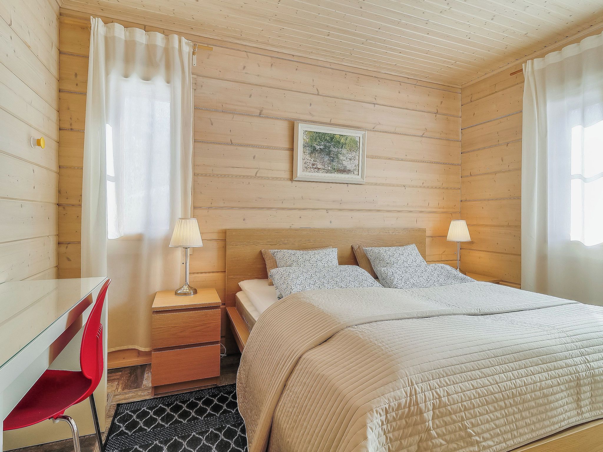 Een slaapkamer met een bed, twee bedlampen, een bureau met een stoel en een ingelijste foto aan de muur.