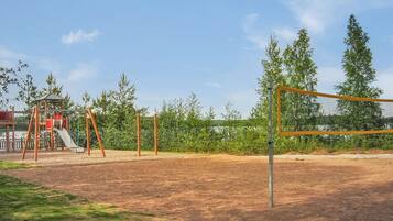 A playground with swings and a slide, surrounded by trees and a clear sky.