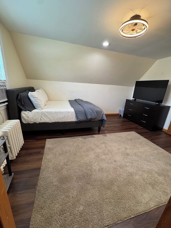 Un dormitorio con cama, televisor, cómoda y radiador.