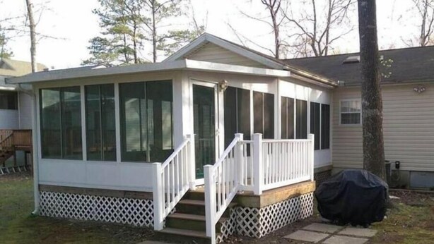 Un espace extérieur abrité doté d’une terrasse en bois, d’une rambarde blanche et d’un escalier menant à une porte.