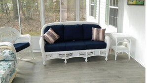 Une pièce avec un canapé bleu foncé, des fauteuils en osier blancs et une petite table blanche.