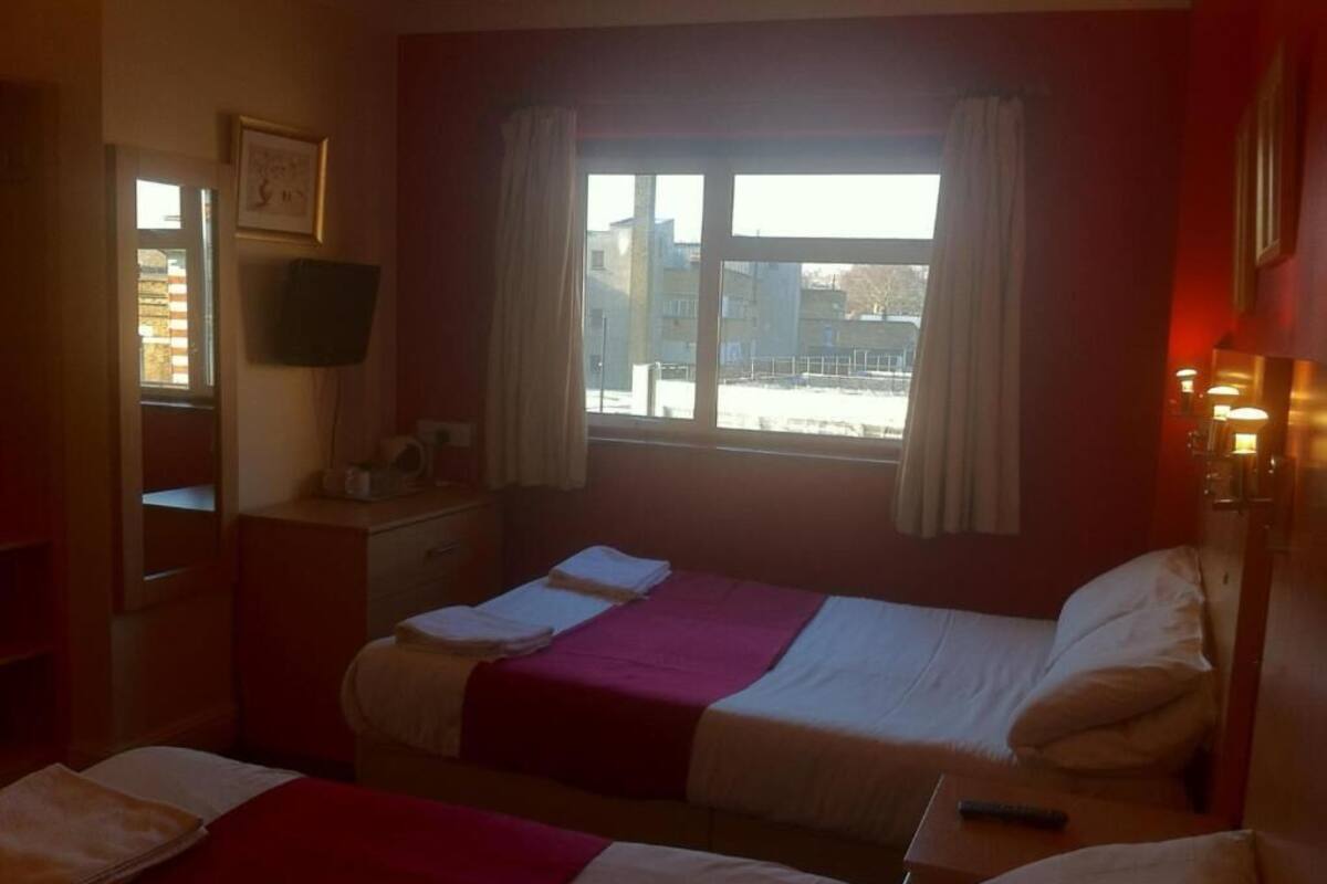 Quarto de hotel com duas camas, televisão, janela com cortinas e vista para o exterior.