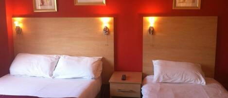 A hotel room with two beds, each with white linens and a red bedspread. There are two bedside tables with lamps, and the walls are painted red.