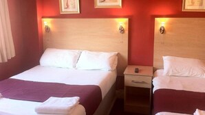 Une chambre d’hôtel avec deux lits, chacun doté d’une tête de lit en bois et de lampes de chevet. Des tableaux encadrés sont accrochés au mur au-dessus des lits.