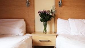 Une chambre d’hôtel avec deux lits simples, une table de chevet en bois avec un tiroir et un vase avec des fleurs.