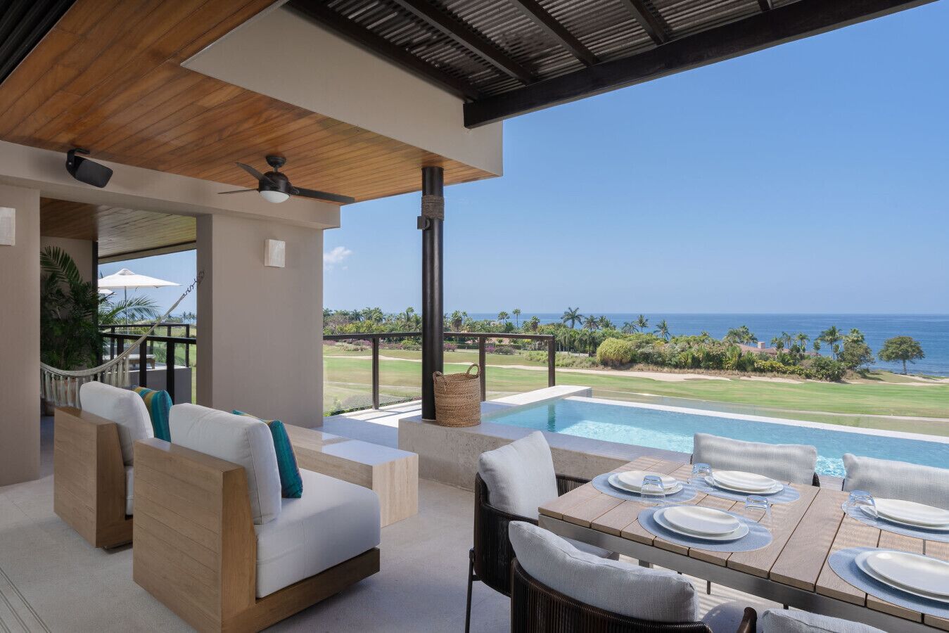 Un espace extérieur moderne aménagé avec des sièges et une piscine, offrant une vue sur un terrain de golf et l’océan.