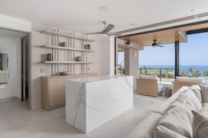 Een moderne keuken met een marmeren kookeiland, houten planken en uitzicht op zee.