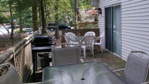 A covered patio with a table and chairs, a grill, and a view of the surrounding trees and a parked car. - Charming 3-bedroom house with AC and WiFi in Ocean Pines (Ocean Pines)