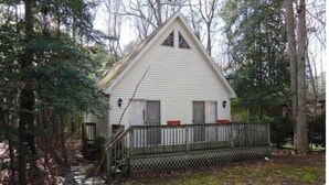 A small, white, single-story house with a gabled roof, surrounded by trees and a wooden fence. - Charming 3-bedroom house with AC and WiFi in Ocean Pines (Ocean Pines)