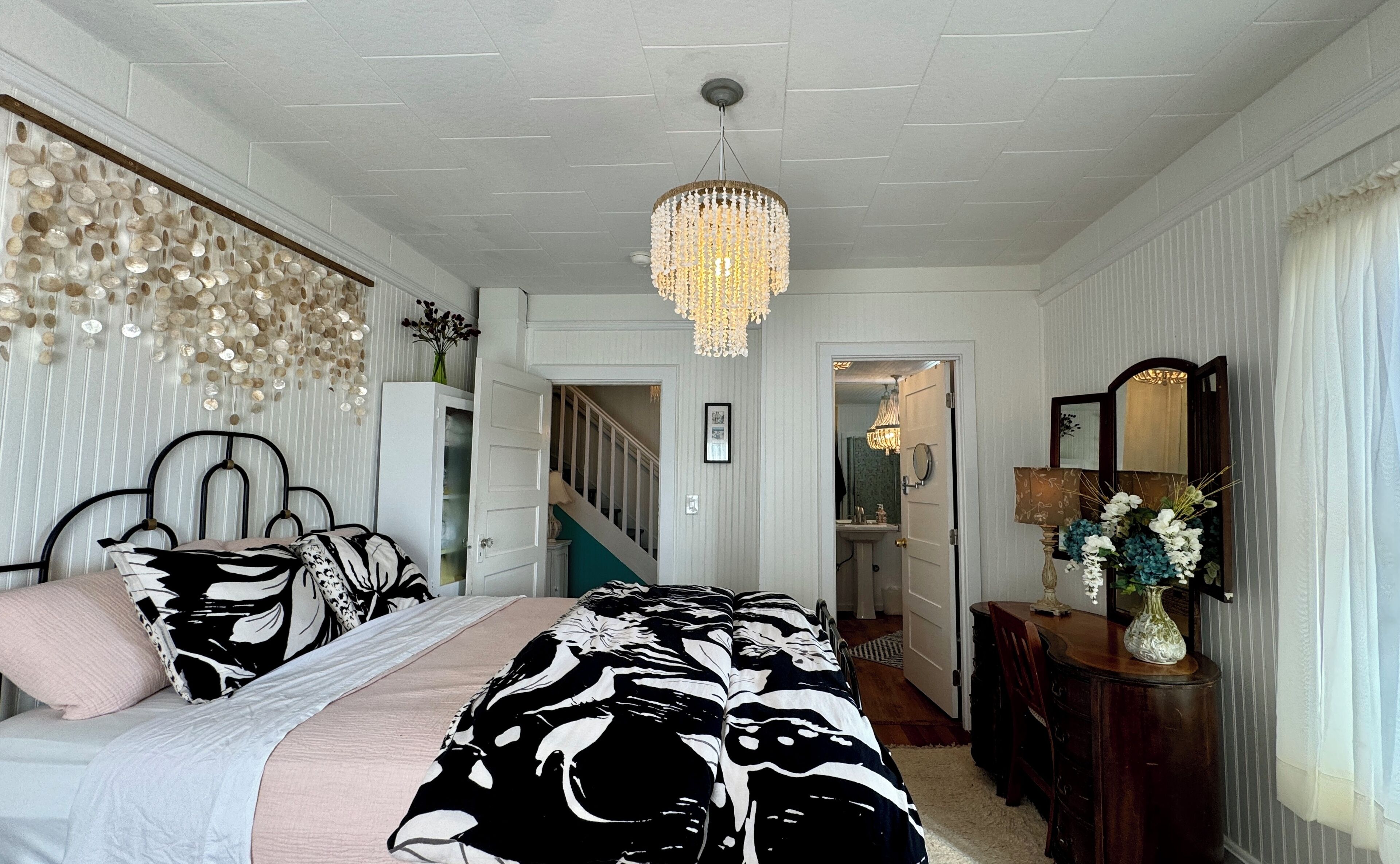 A bedroom with a bed, a chandelier, a mirror, and a dresser.