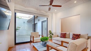 A modern living room with a sofa, armchairs, and a coffee table. There is a ceiling fan, a TV mounted on the wall, and a sliding glass door leading to an outdoor area. - Brand new modern home w pool- perfect for groups (Sayulita)
