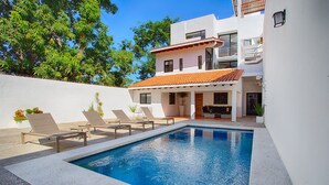 A swimming pool with lounge chairs, a covered patio, and a white building with a red-tiled roof. - Brand new modern home w pool- perfect for groups (Sayulita)