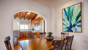 A dining area with a wooden table and chairs, a kitchen in the background, and a large abstract painting on the wall. - Brand new modern home w pool- perfect for groups (Sayulita)