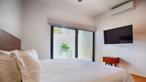 A bedroom with a large bed, a TV mounted on the wall, and a potted plant near the window. - Brand new modern home w pool- perfect for groups (Sayulita)