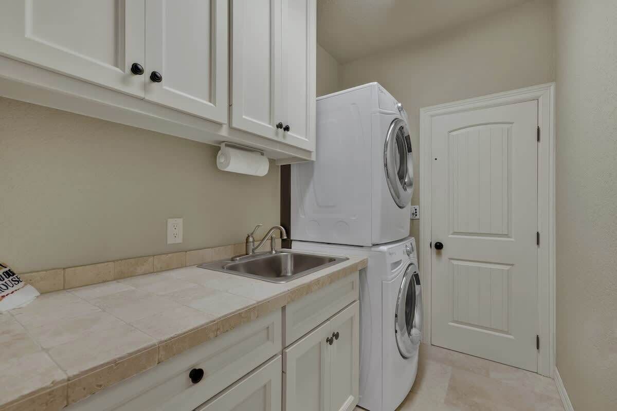 A kitchen with white cabinets, a stainless steel sink, and a stacked washer and dryer.