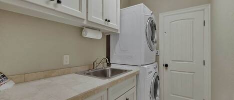 A kitchen with white cabinets, a stainless steel sink, and a stacked washer and dryer.