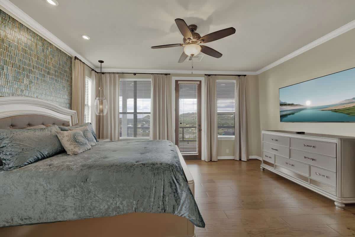 Un dormitorio con cama, ventilador de techo, televisor y vista a un paisaje por la ventana.