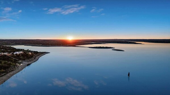 A calm lake with a sunset, a small island, and a distant shoreline with buildings. - Canyon Lakehouse Panoramic Lake Views With Firepit! (Canyon Lake)