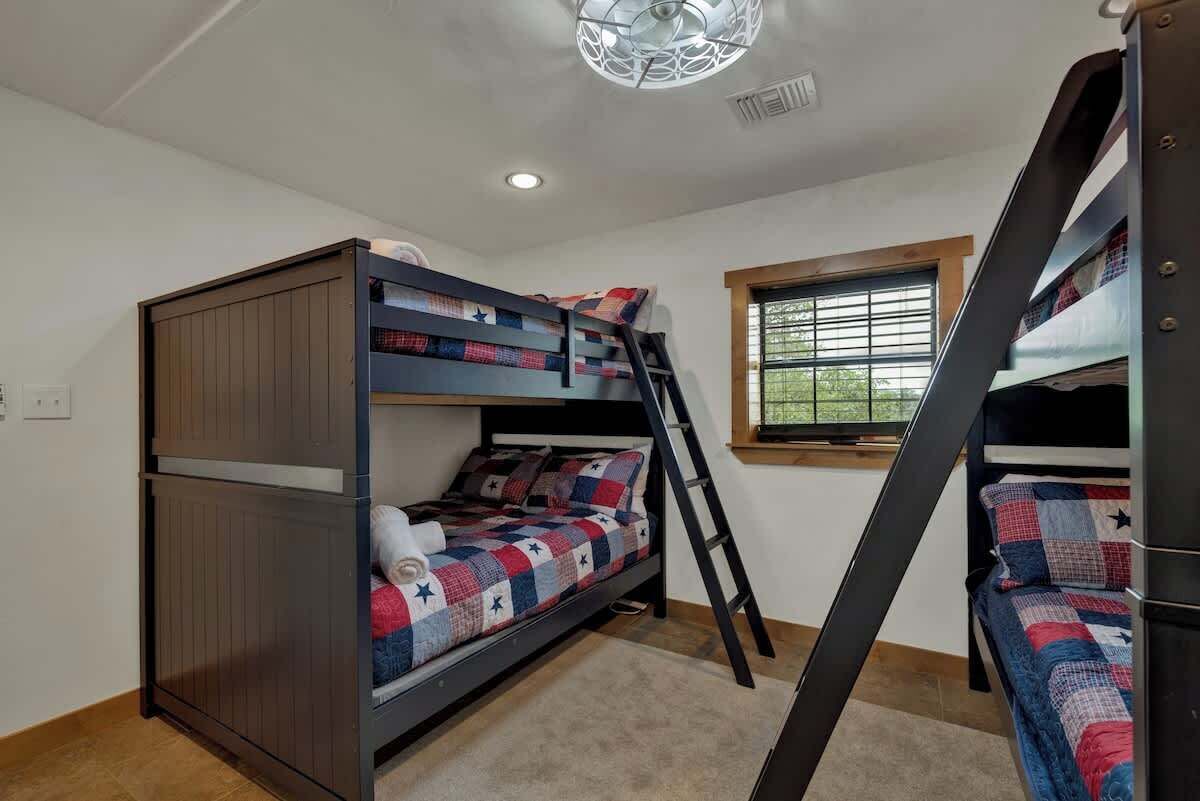 A bunk bed room with a ladder, a window with blinds, and a ceiling light fixture.