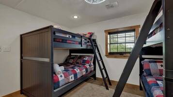 A bunk bed room with a ladder, a window with blinds, and a ceiling light fixture.