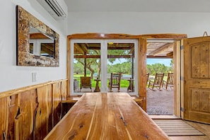 A wooden dining table with a view of outdoor seating and a wooden door.