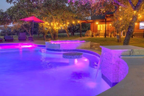 A swimming pool with a stone edge and a hot tub, surrounded by lounge chairs and a covered seating area.