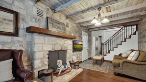 A rustic living room with stone walls, a fireplace, a wooden rocking horse, and a staircase. - Rocking Ox Gasthaus-5 Minutes to Downtown! (Fredericksburg)