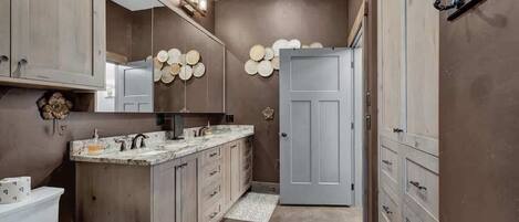 A modern bathroom with a marble vanity, a large mirror, and a door leading to another room.