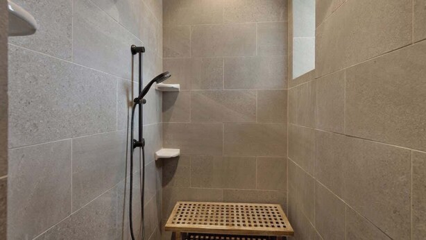 A small, tiled shower area with a wooden bench and a handheld showerhead. - West End Lodge Resort Style Pool! (Fredericksburg)