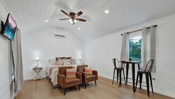 A room with a bed, two armchairs, a table with chairs, a ceiling fan, and a window with curtains. - Cates Cottage in the Hill Country 8 Mins to Fred! (Fredericksburg)