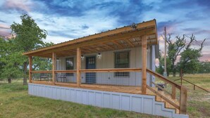 A single-story wooden structure with a covered porch, a staircase, and a fenced area. - Cates Cottage in the Hill Country 8 Mins to Fred! (Fredericksburg)