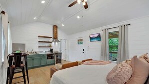 A spacious room with a large bed, a dining area, and a kitchen. - Cates Cottage in the Hill Country 8 Mins to Fred! (Fredericksburg)