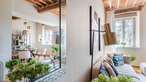Un salon moderne avec un canapé, un coin repas comprenant une table et des chaises, et une grande fenêtre donnant sur un paysage arboré.