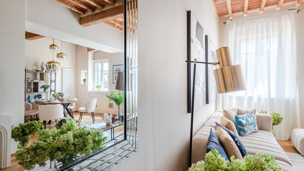 Un salon moderne avec un canapé, des coussins décoratifs, un miroir et un coin repas comprenant une table et des chaises.