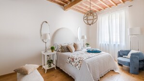 Une chambre à coucher comprenant un lit, des tables de chevet, une chaise et un luminaire suspendu.