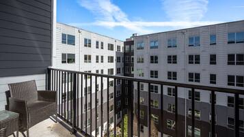 A balcony with wicker furniture, overlooking a multi-story building with large windows and a clear sky.