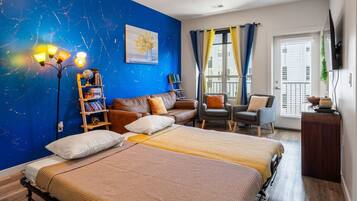 A bedroom with two beds, a bookshelf, a sofa, a chair, and a TV.