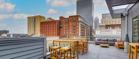 A rooftop terrace with tables and chairs, offering a view of city buildings.
