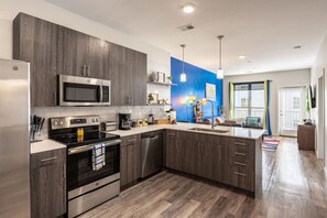 A modern kitchen with dark wood cabinets, stainless steel appliances, and a blue accent wall.