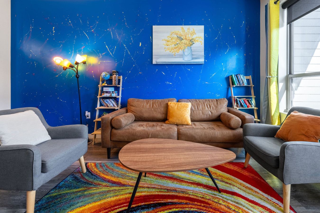 Un salón con pared azul, un sofá marrón, una mesita de centro y una alfombra colorida.