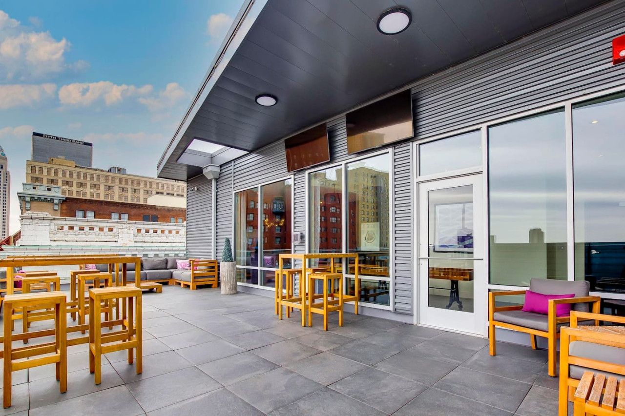 Una terraza en la azotea con mobiliario exterior, ventanas amplias y vistas del horizonte de la ciudad.